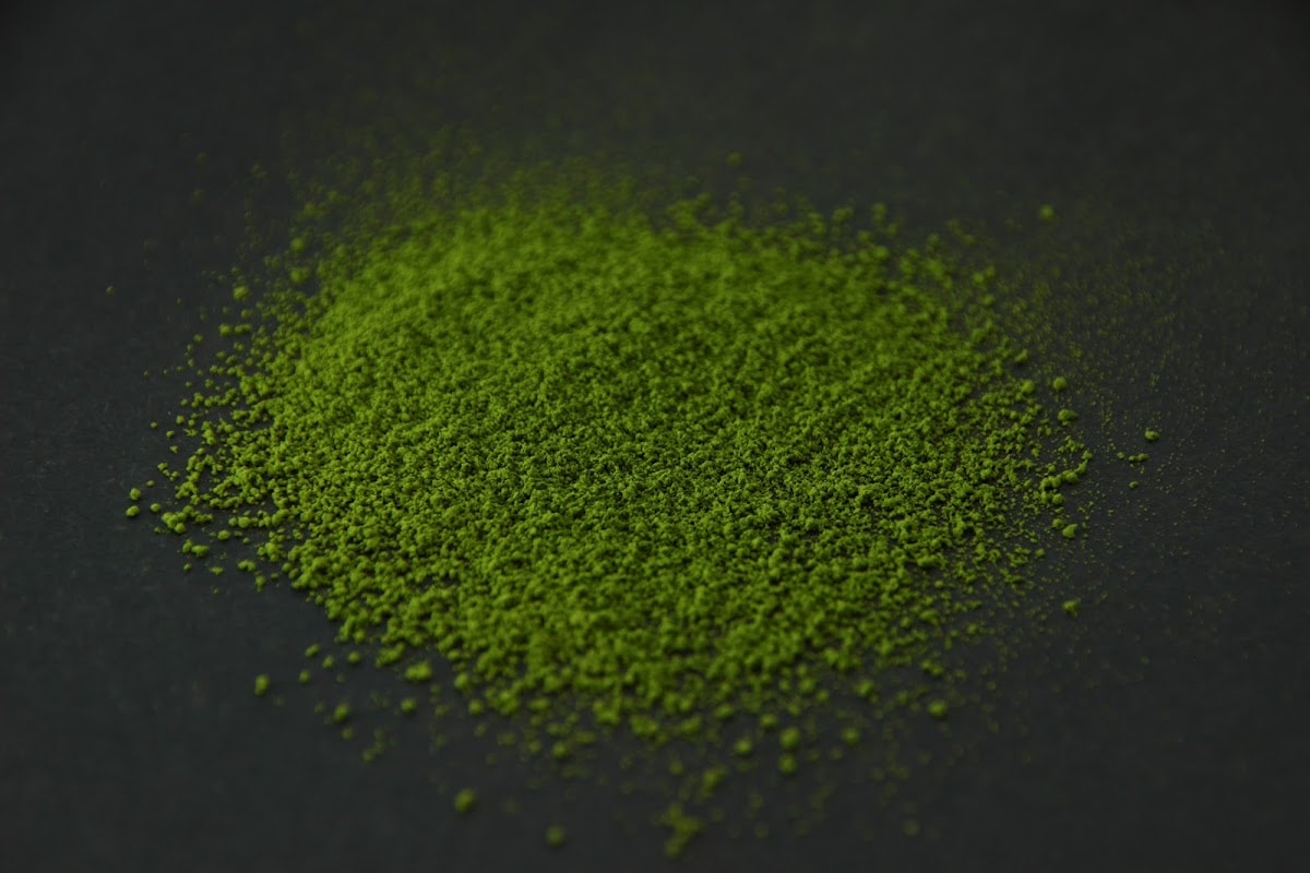 Bright green SR-8 matcha powder heaped on a dark surface