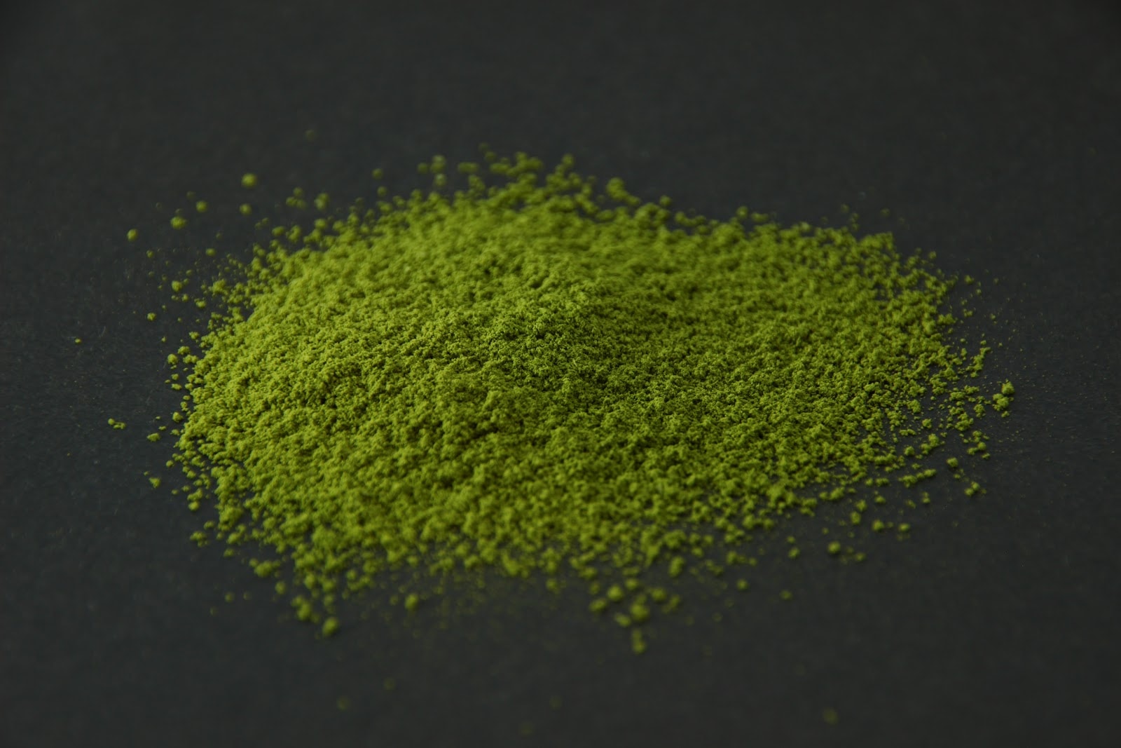 A heap of bright green matcha powder on a dark surface
