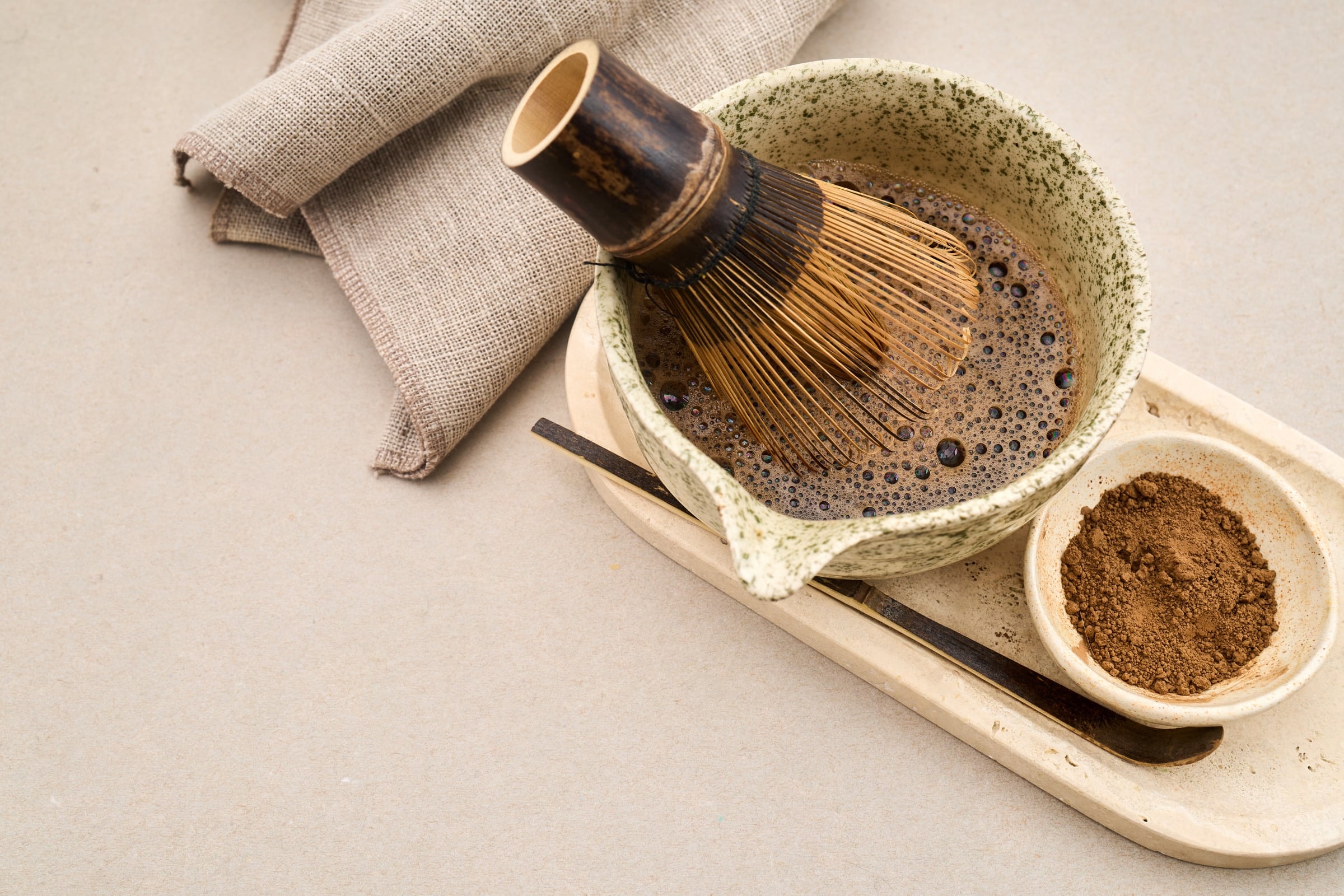 A bamboo whisk resting in a bowl of whisked matcha on a wooden tray